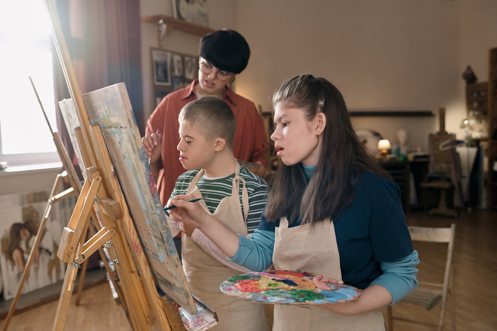 Two Children with Disability Painting on Easels in Art Class And Teacher